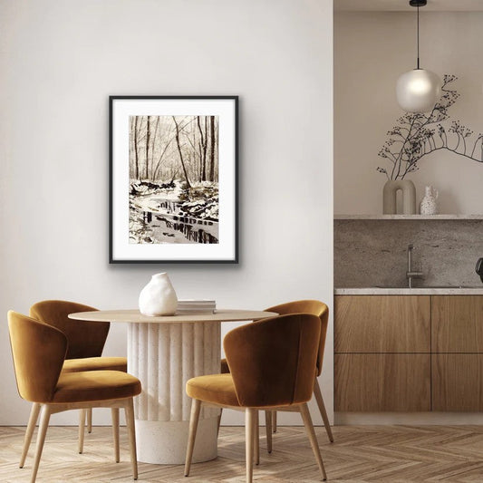 Serene watercolour painting of a snowy winter stream with bare trees and wooden bridge displayed in a modern dining room by Canadian watercolour artist Brigitte Klassen